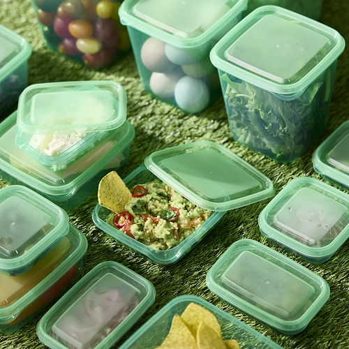 Recipientes de plástico verde con tapa, algunos llenos de comida, sobre superficie texturizada.
