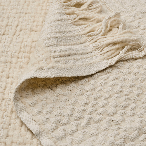 Primer plano de la manta de crema tejida que muestra textura y calidad. Un lado lana, otro lado algodón. Tejido a mano, suave, aspecto natural.