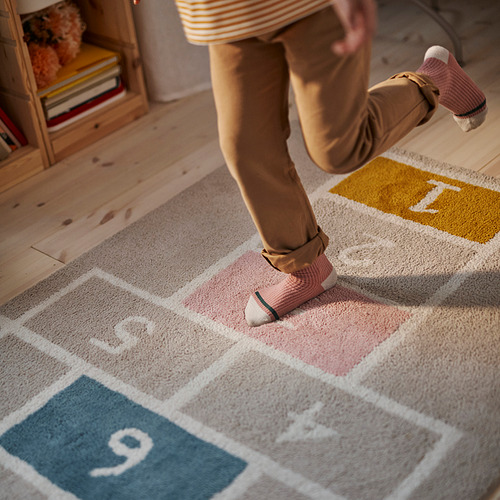 Un niño juega en una colorida alfombra de rayuela, pisando números, mejorando el equilibrio y la coordinación.
