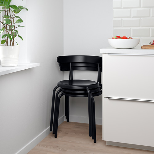 Sillas negras apiladas cerca de un armario blanco con un cuenco de frutas. Ideal para ahorrar espacio.