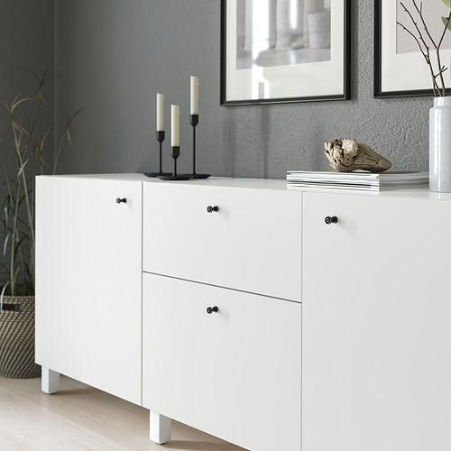 Mueble blanco con pomos negros; La parte superior sostiene velas, libros y conchas.