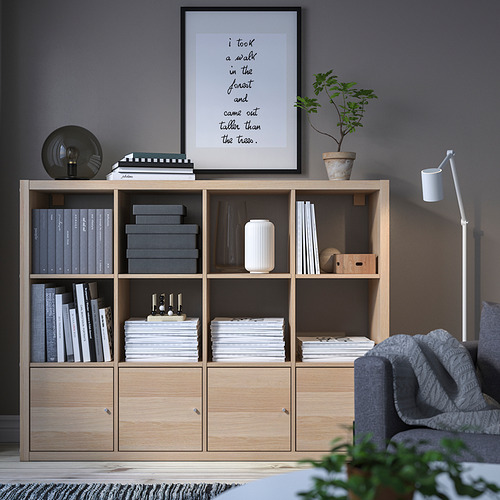 Sala de estar moderna con estanterías KALLAX, libros, decoración, silla gris y plantas.