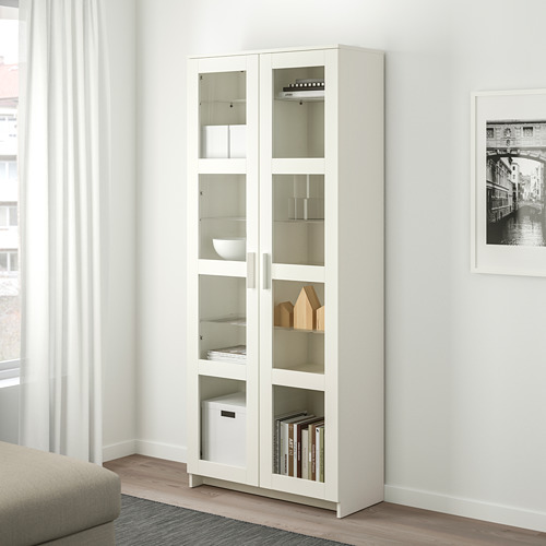 White BRIMNES glass-door cabinet. Tall, slim, modern design fits books, decor. Shelf displays items clearly while protecting them.