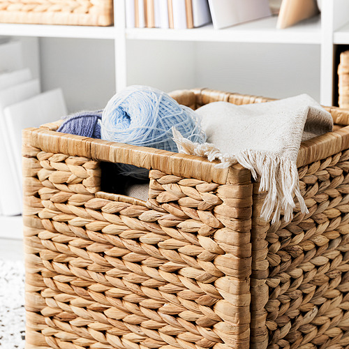 Cesta de jacinto natural tejida a mano con hilo azul claro, manta blanca, en estante blanco.