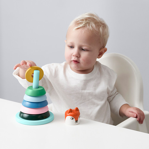 Un niño pequeño juega con un anillo de juguete apilable en una silla alta, mejorando sus habilidades motoras y aprendiendo formas y colores.