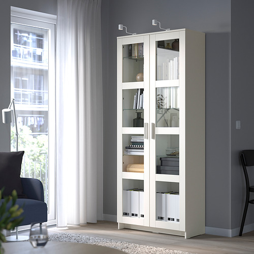 BRIMNES glass-door cabinet with adjustable shelves, near large windows.