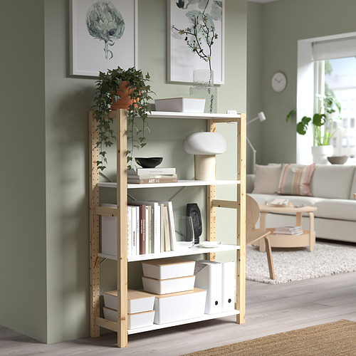 Estantería de madera clara, cajas blancas KUGGIS, planta verde, ambiente de salón. Pequeña caja KUGGIS apilada en el estante inferior.