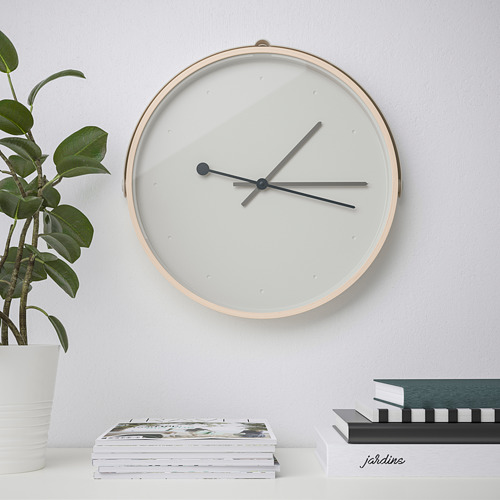Moderno reloj de pared silencioso con manecillas delgadas, debajo del estante con libros y plantas.