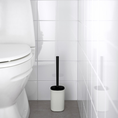 Escobilla de baño blanca en soporte negro junto a un inodoro en un baño minimalista.