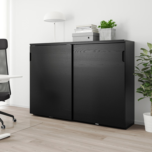 Mueble negro GALANT, delgado, alto, con puertas correderas, en ambiente de oficina con plantas y silla.