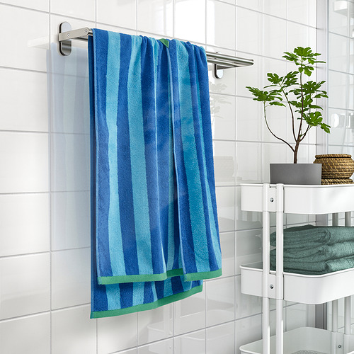 La toalla de rayas azules y verdes cuelga en un estante, rodeada de azulejos blancos y almacenamiento.