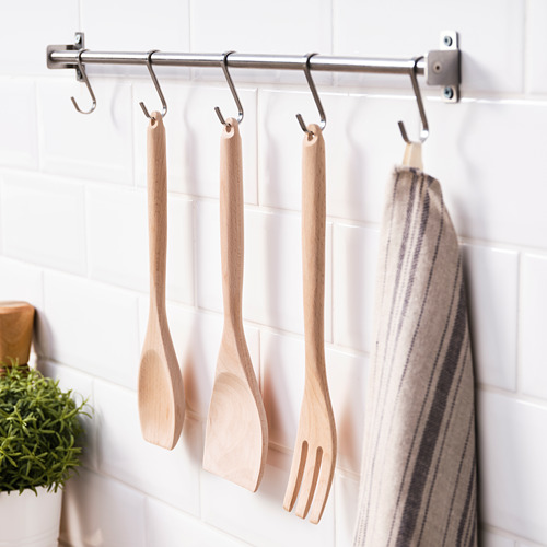 La varilla de acero inoxidable con ganchos en S sostiene utensilios de cocina de madera y toalla a rayas en la pared de azulejos blancos.
