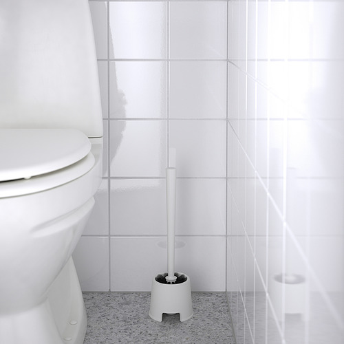 Una escobilla de baño blanca, BOLMEN, se encuentra junto a un inodoro en un suelo moteado, lista para limpiar.