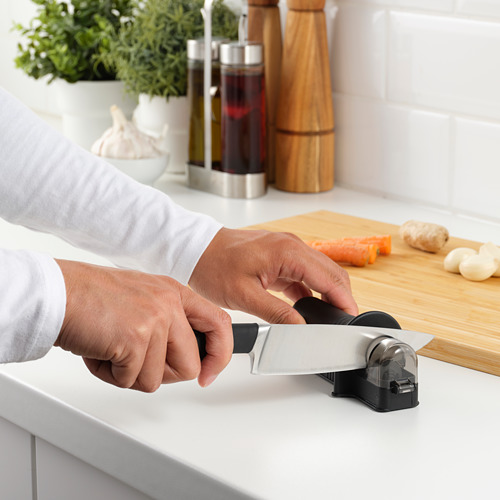 La persona afila el cuchillo en un dispositivo en la cocina, con ingredientes cerca.