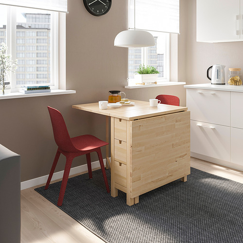 Pequeña mesa de madera con sillas rojas en el rincón de la cocina. Madera clara, diseño minimalista, encaja perfectamente debajo del mostrador.