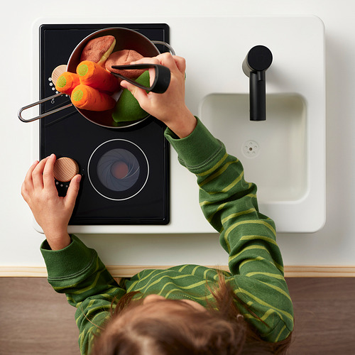 Niño jugando con estufa de juguete, cortando verduras en una estufa de juguete negra con fregadero y grifo.