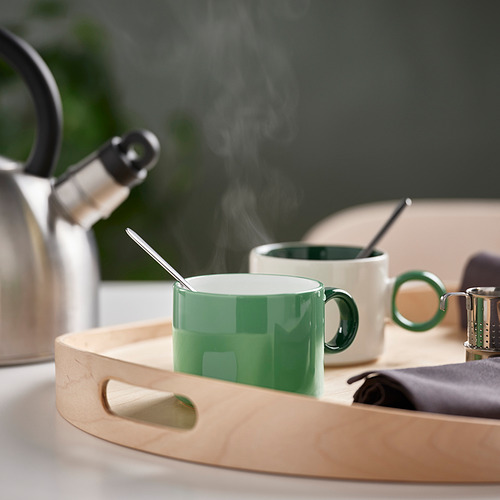 La bandeja de madera contiene tazas verdes y blancas, cuchara, servilleta y hervidor de vapor.