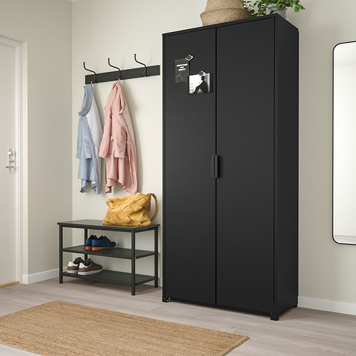 Mueble BROR negro con 2 puertas en la habitación, rodeado de zapatero y perchero.