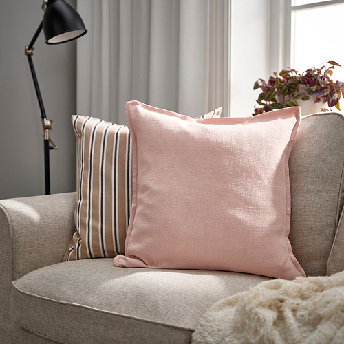 Acogedora sala de estar con sofá gris, dos almohadas LAGERPOPPEL de color rosa claro, una a rayas, otra sólida, cerca de una lámpara y una ventana.