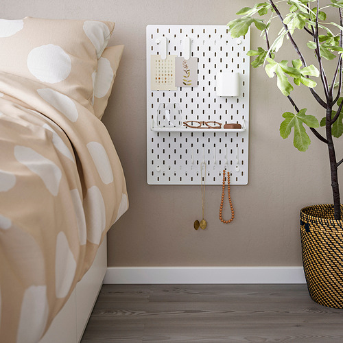 Tablero perforado SKÅDIS con accesorios cerca de la cama y la planta.