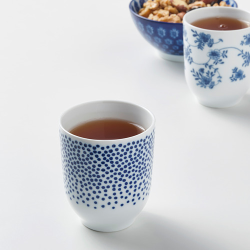 Dos tazas de té estampadas en azul y blanco, una floral y otra punteada, cerca de un plato de bocadillos.
