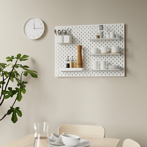 Tablero perforado de pared SKÅDIS con estantes y utensilios de cocina; reloj y planta cerca.