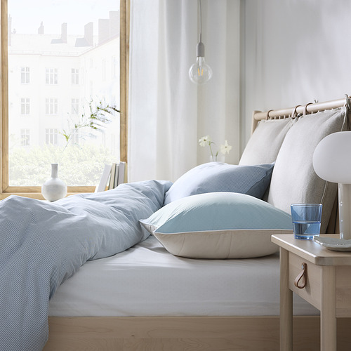 Dormitorio minimalista: cama azul con almohadas blancas, mesita de noche de madera, bombilla colgante, vista a la ciudad.