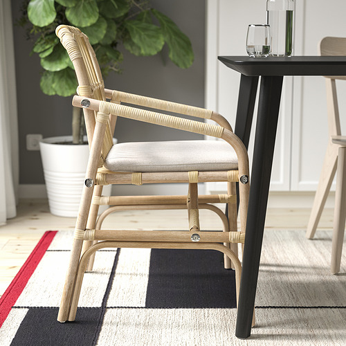 Silla con respaldo de ratán tejido, cojín ligero, cerca de mesa negra y planta.