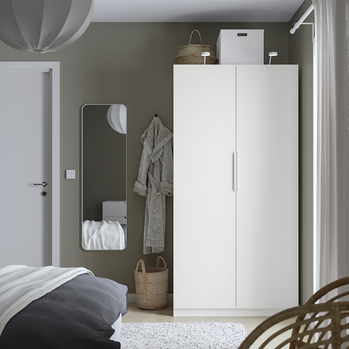 Minimalist bedroom featuring a white PAX wardrobe, tall and slim closet near a bed, gray wall, mirror, and hanging robe.