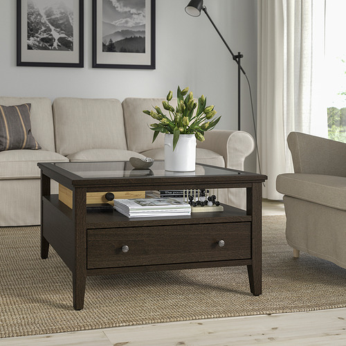 Sala de estar moderna con mesa de centro de madera oscura, sofá y sillón. La mesa contiene revistas y un jarrón. Fotos en blanco y negro en la pared.