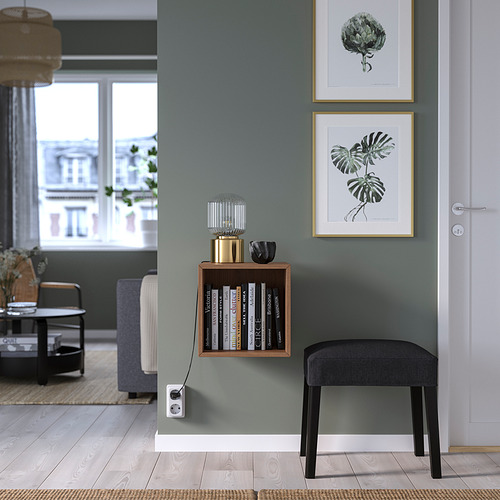 Armario de pared de madera EKET con libros, entre impresiones artísticas, taburete gris debajo.