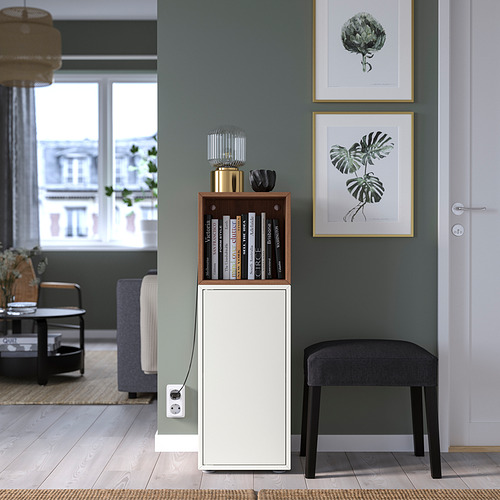 Sala de estar moderna con gabinete blanco EKET, taburete negro, pared verde, estampados de plantas enmarcadas, sofá azul y piso de madera.