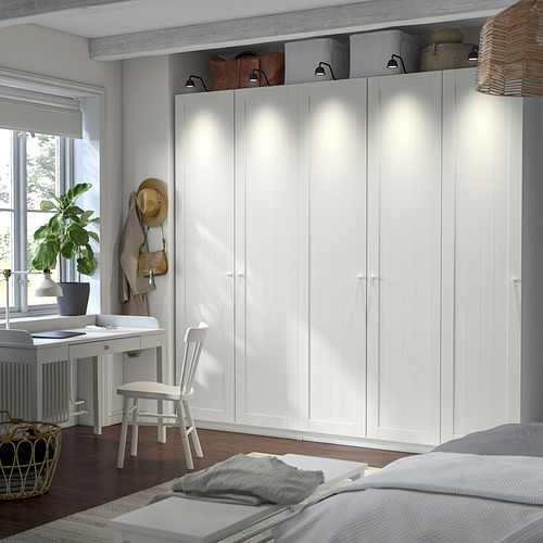 Un gran armario blanco con puertas altas destaca contra las paredes de color gris claro. Su tamaño eclipsa al escritorio y la silla cercanos.