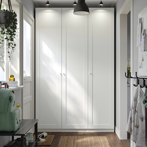 A white PAX wardrobe, tall and sleek, with closed doors. Its the main furniture, larger than surrounding items, with hanging lights above.