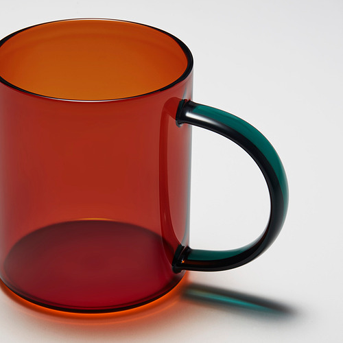 Taza de vidrio transparente de color rojo brillante con asa negra resistente. La luz del sol proyecta una sombra clara.