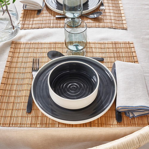 Mesa con cuenco de cerámica gris sobre plato blanco, vaso y cubiertos.
