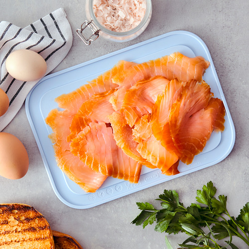 Una bandeja azul contiene salmón ahumado en rodajas, entre otros alimentos, en un mostrador.