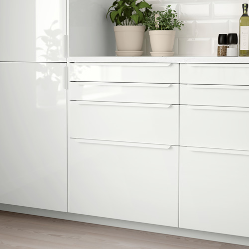 Modern white high-gloss kitchen cabinet with sleek, straight lines; three drawers, smaller than surrounding items.