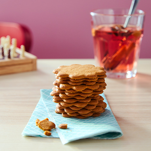 Pila de galletas de jengibre en una servilleta azul, un vaso de bebida roja, un juguete de madera detrás.