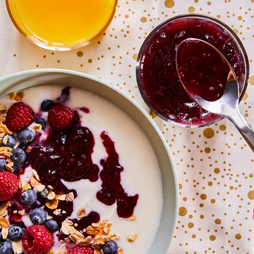 Parfait de yogur con granola, frutos rojos, mermelada, cuchara, bebida cítrica.