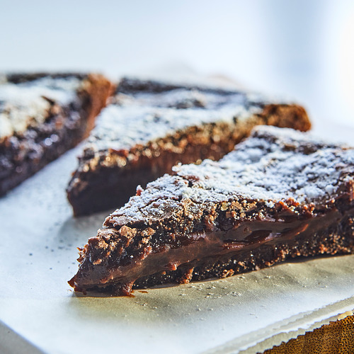 Dos rebanadas de pastel de chocolate pegajoso en un plato blanco, espolvoreado con azúcar en polvo.