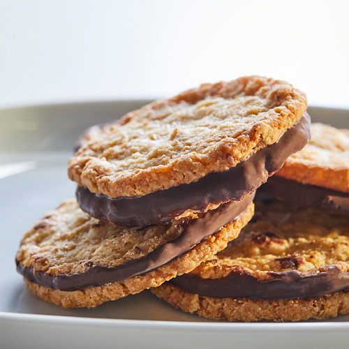 Galletas de avena de color marrón dorado apiladas con relleno de chocolate negro en un plato blanco.