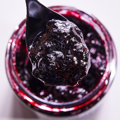 Un frasco de mermelada orgánica de arándanos oscuros con una cucharada encima.