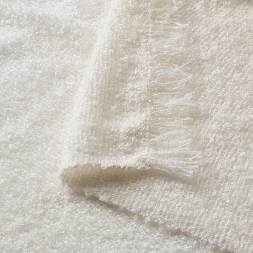 Primer plano de una manta suave, texturizada y de color blanco roto con detalles de punto arrugado y flecos.