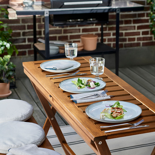 Mesa de comedor de exterior de madera con platos, tenedores y vasos, ideal para fiestas de verano.