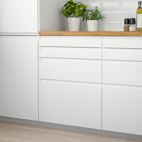 Cocina moderna con cajones y gabinetes VOXTORP blancos, manijas elegantes y plantas en macetas sobre encimera de madera.