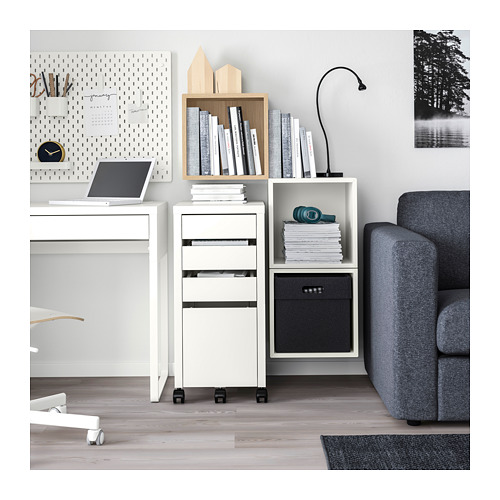 Moderna configuración de oficina con unidad de almacenamiento EKET blanca, sofá gris, computadora portátil, decoraciones de madera y libros.