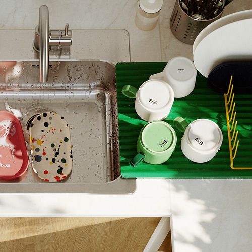 Fregadero de acero inoxidable con estante para platos verde que sostiene recipientes de colores, mostrando la organización y el secado de la cocina.