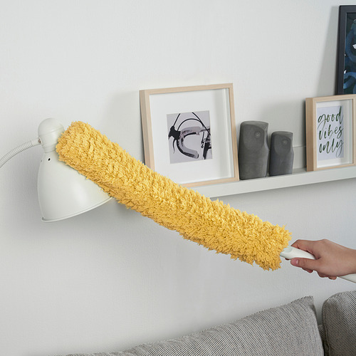 Una persona utiliza un plumero de microfibra PEPPRIG para limpiar el polvo de una estantería de la pared. La cubierta de los plumeros es amarilla, efectiva para áreas grandes.