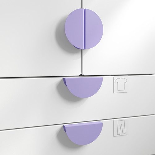 Tres tiradores BEGRIPA morados sobre cajones blancos. El mango superior es circular, los mangos laterales son semicirculares. Diseño de fácil agarre para niños.
